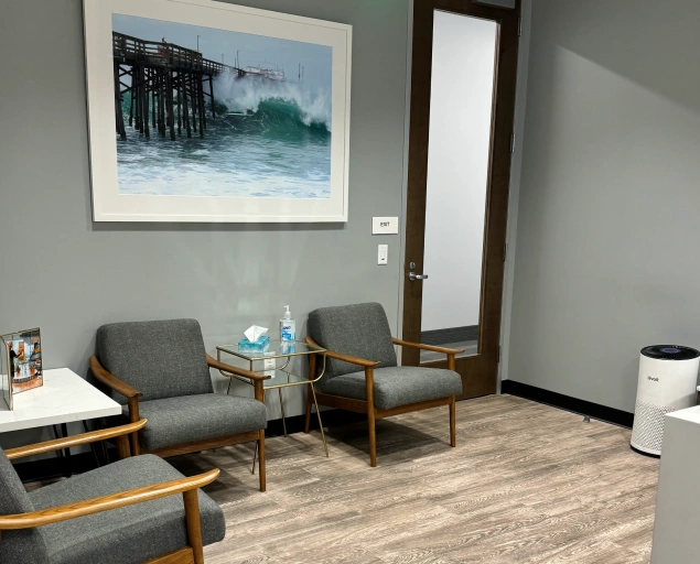 Modern dental office waiting room with gray chairs, wooden accents, and coastal artwork on wall.