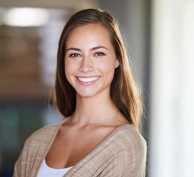 Professional headshot of smiling woman in beige cardigan against blurred office background.