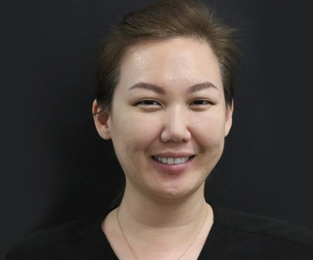 Smiling woman in professional headshot against dark background for dental practice website.