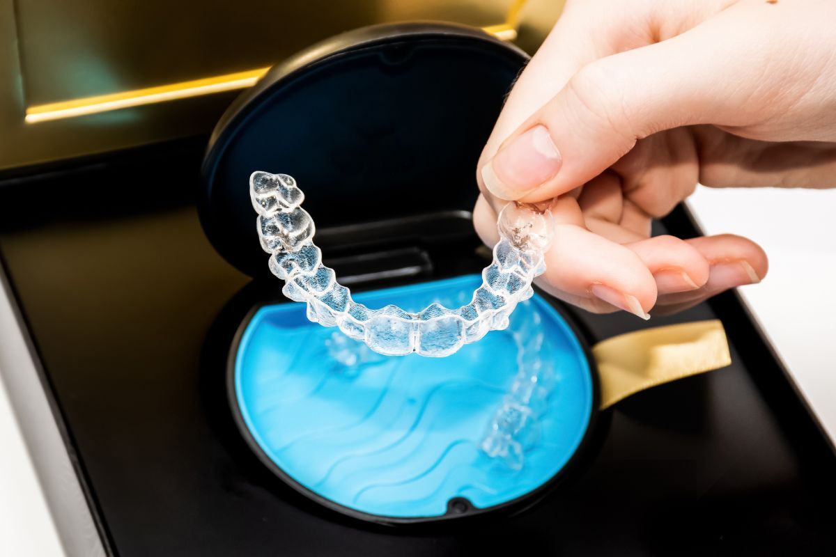 Person holding clear Invisalign aligner over blue cleaning solution container.