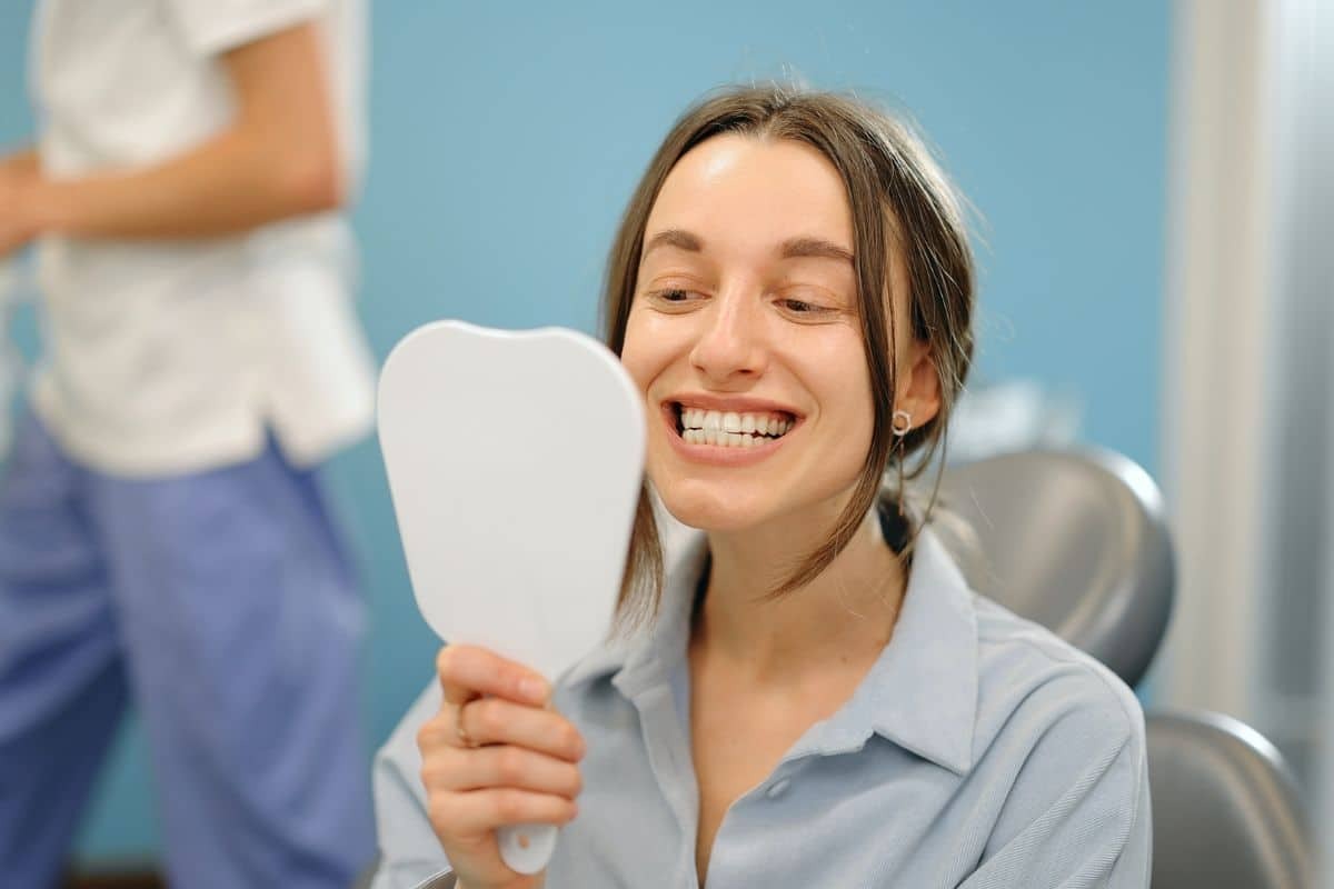 Happy dental patient admiring her smile in mirror at Newport Beach periodontal practice.